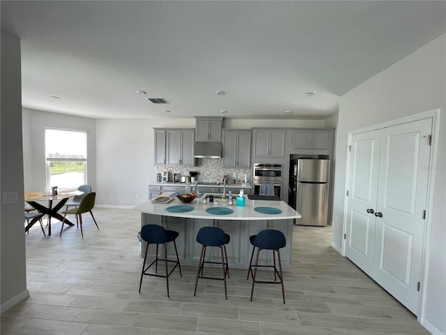 kitchen featuring gray cabinetry, a center island with sink, a breakfast bar, and appliances with stainless steel finishes