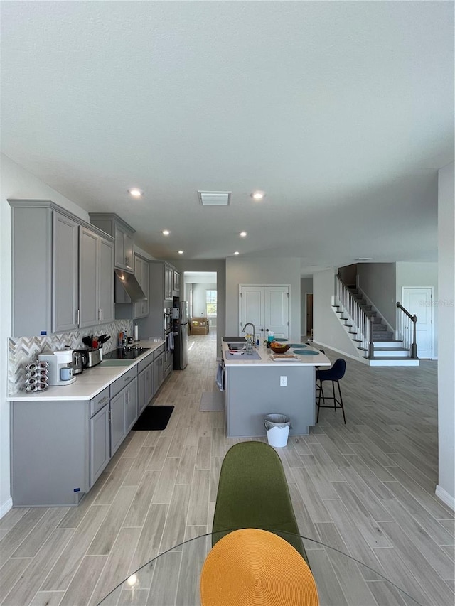 kitchen featuring sink, a breakfast bar area, gray cabinetry, an island with sink, and decorative backsplash