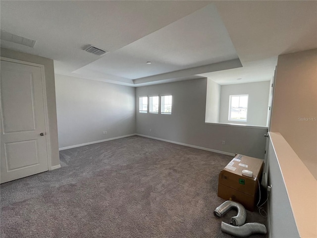 spare room with a raised ceiling, dark colored carpet, and plenty of natural light