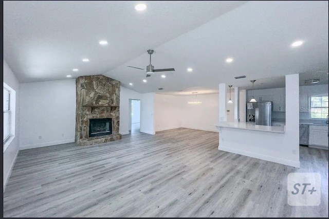 unfurnished living room featuring vaulted ceiling, ceiling fan, a fireplace, and light hardwood / wood-style flooring