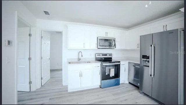 kitchen with appliances with stainless steel finishes, sink, white cabinets, and light hardwood / wood-style flooring