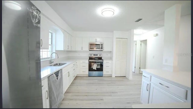 kitchen featuring appliances with stainless steel finishes, light hardwood / wood-style floors, sink, and white cabinets