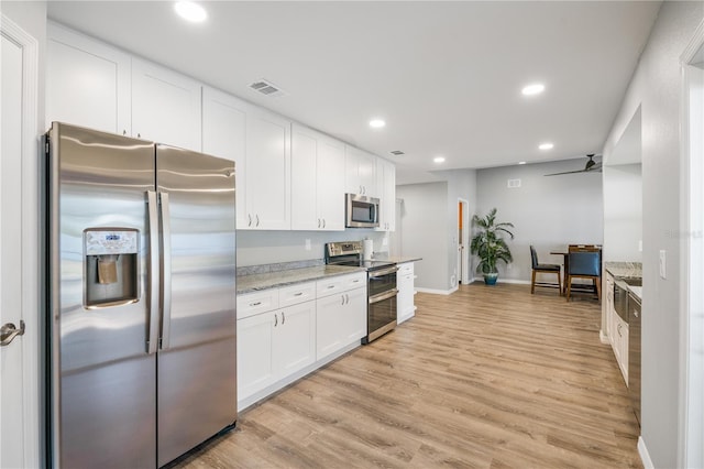 kitchen featuring light stone counters, stainless steel appliances, white cabinets, and light wood-type flooring