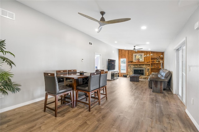 dining space with a stone fireplace, wood-type flooring, and ceiling fan