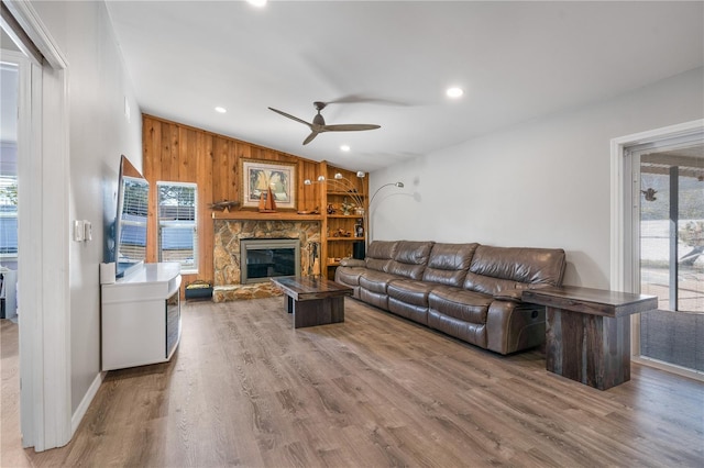 living room with ceiling fan, a stone fireplace, vaulted ceiling, and wood-type flooring