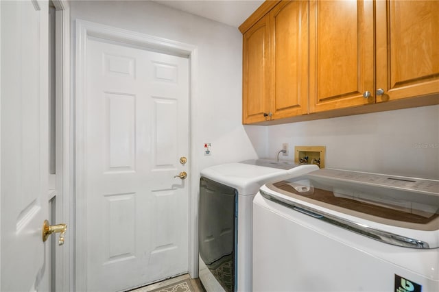 clothes washing area with separate washer and dryer and cabinets