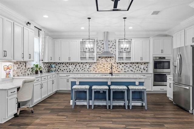 kitchen featuring wall chimney range hood, a breakfast bar, white cabinetry, stainless steel appliances, and a center island with sink