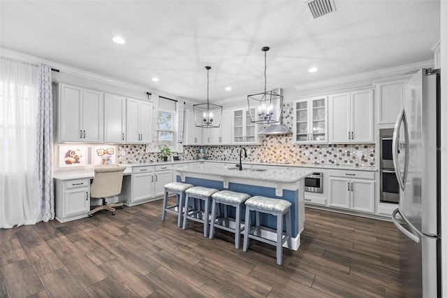 kitchen featuring a kitchen island with sink, white cabinets, stainless steel refrigerator, and a breakfast bar