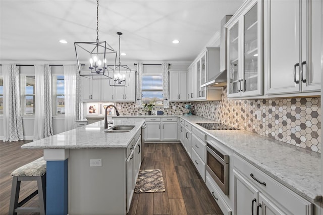 kitchen featuring sink, light stone counters, black electric cooktop, a healthy amount of sunlight, and a kitchen island with sink