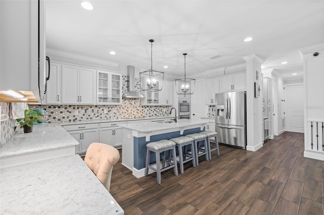 kitchen featuring a breakfast bar, appliances with stainless steel finishes, an island with sink, wall chimney range hood, and white cabinets