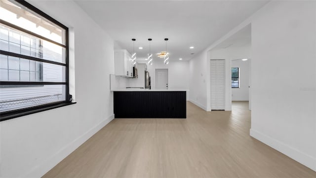 kitchen featuring appliances with stainless steel finishes, hanging light fixtures, light hardwood / wood-style floors, white cabinets, and kitchen peninsula