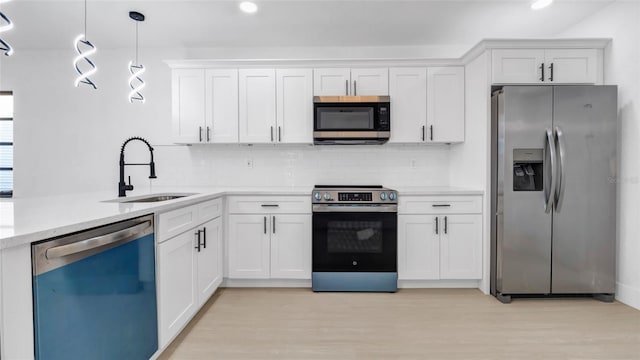 kitchen featuring appliances with stainless steel finishes, decorative light fixtures, white cabinetry, sink, and light hardwood / wood-style floors