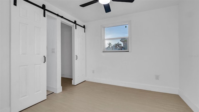 unfurnished bedroom with ceiling fan, a barn door, and light wood-type flooring