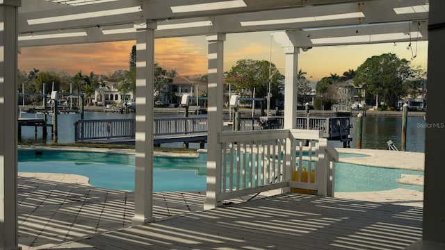 pool at dusk featuring a water view and a jacuzzi