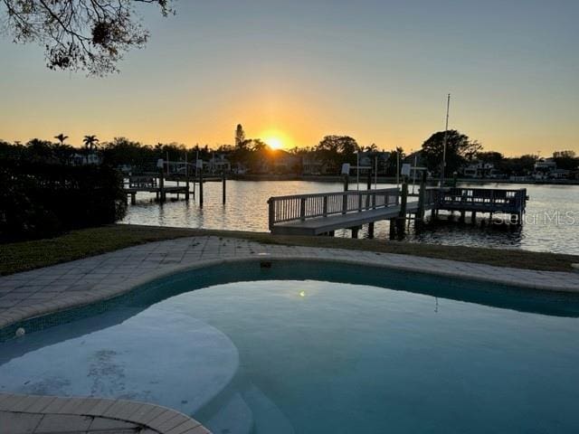 pool at dusk with a water view and a dock