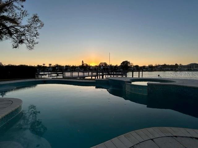 pool at dusk featuring an in ground hot tub