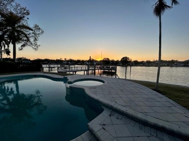 pool at dusk featuring a water view and an in ground hot tub