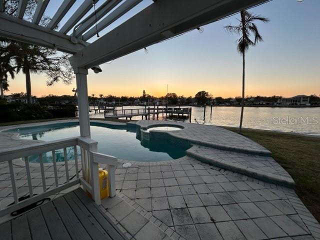 pool at dusk with an in ground hot tub, a patio, and a water view