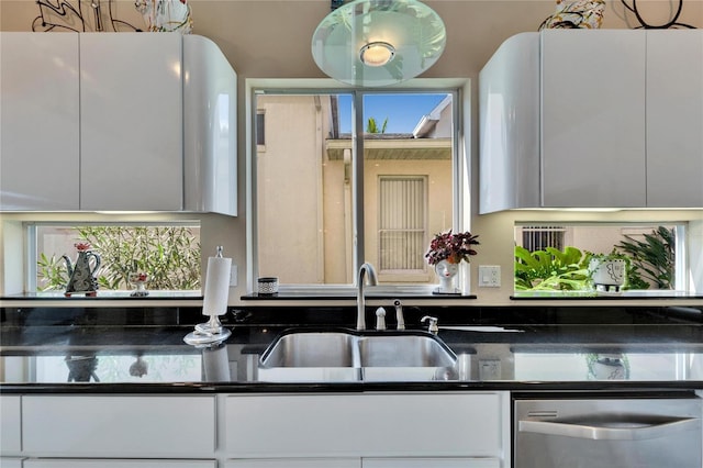 kitchen featuring stainless steel dishwasher, dark stone countertops, sink, and white cabinets