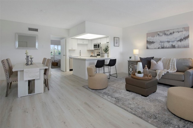 living room with sink, a textured ceiling, and light wood-type flooring