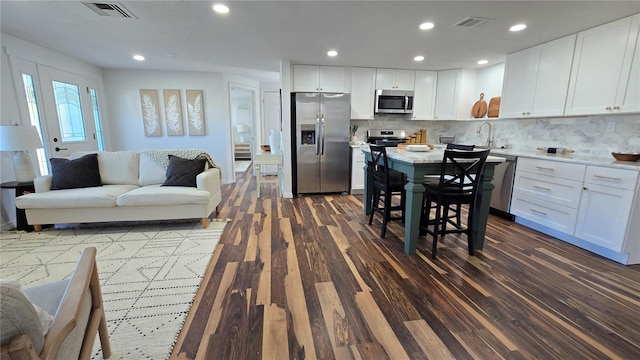 kitchen featuring a breakfast bar, stainless steel appliances, white cabinets, dark hardwood / wood-style flooring, and decorative backsplash