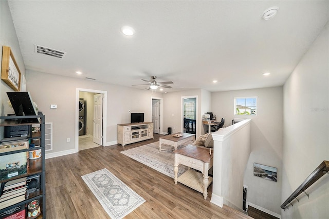 living room featuring ceiling fan, stacked washer / dryer, and light wood-type flooring