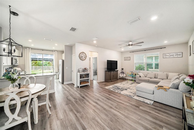 living room with ceiling fan with notable chandelier and hardwood / wood-style floors