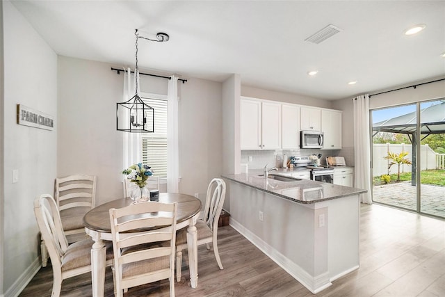 kitchen with kitchen peninsula, pendant lighting, stainless steel appliances, light stone countertops, and white cabinets