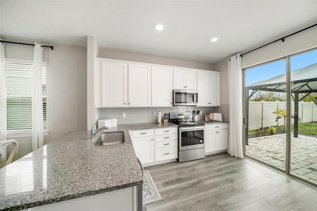 kitchen featuring stone counters, sink, white cabinets, stainless steel appliances, and light wood-type flooring