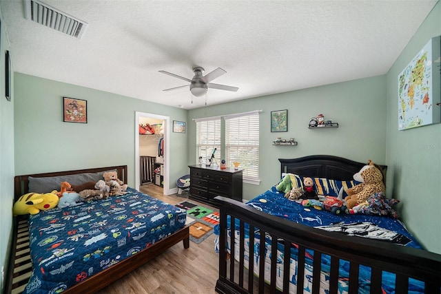 bedroom featuring light hardwood / wood-style flooring, a spacious closet, ceiling fan, a textured ceiling, and a closet