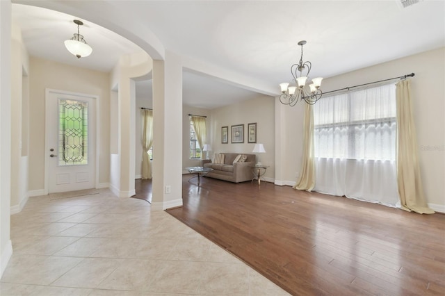 foyer with arched walkways, light wood-type flooring, baseboards, and a notable chandelier