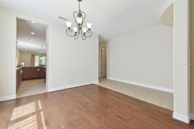 unfurnished dining area featuring light wood-type flooring, baseboards, visible vents, and a notable chandelier