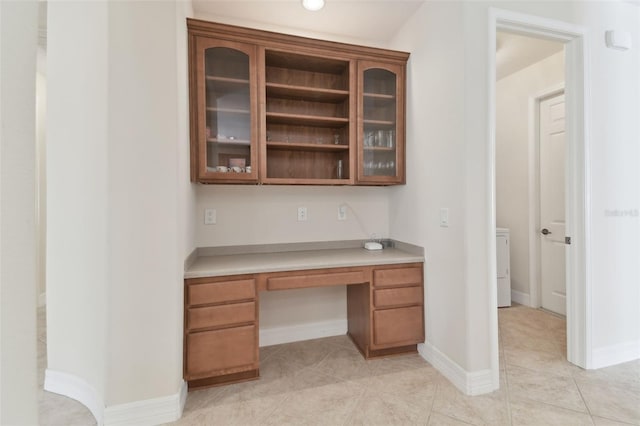 unfurnished office featuring light tile patterned floors, built in desk, and baseboards