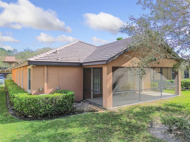 rear view of house featuring a sunroom, a yard, a tiled roof, and stucco siding