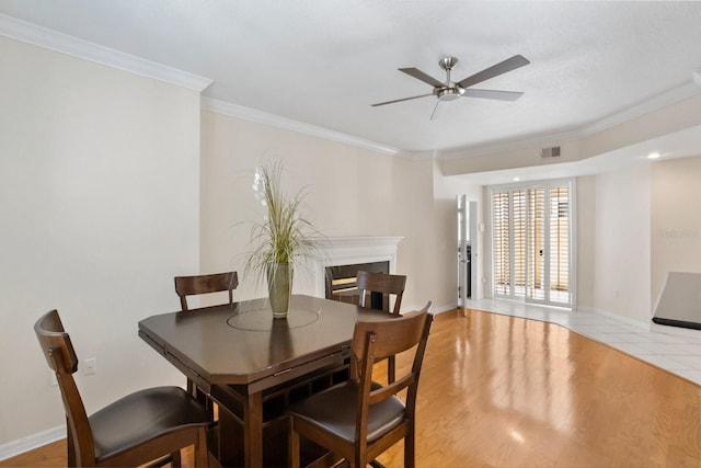 dining space featuring crown molding, a high end fireplace, ceiling fan, and light wood-type flooring