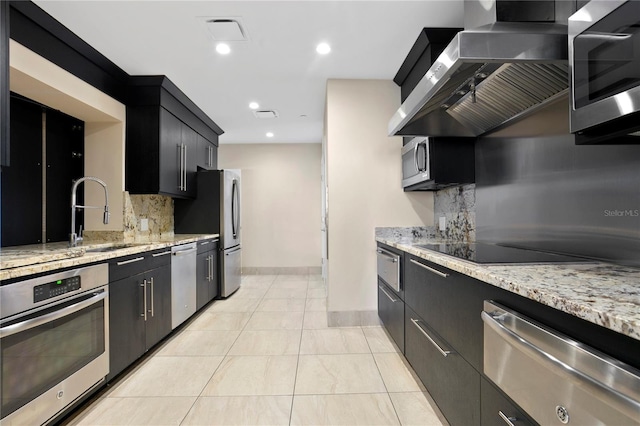 kitchen with wall chimney range hood, sink, appliances with stainless steel finishes, backsplash, and light stone countertops