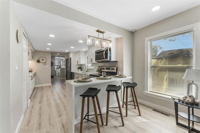 kitchen with hanging light fixtures, stainless steel appliances, white cabinets, decorative backsplash, and kitchen peninsula