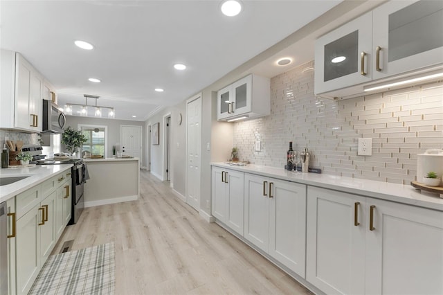 kitchen with light hardwood / wood-style flooring, appliances with stainless steel finishes, tasteful backsplash, white cabinets, and decorative light fixtures