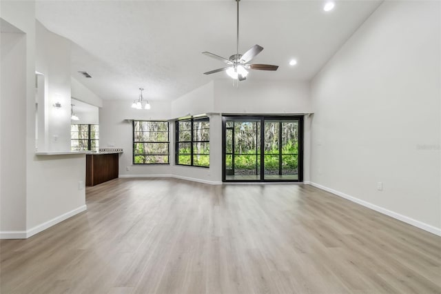 unfurnished living room featuring ceiling fan with notable chandelier, high vaulted ceiling, and light wood-type flooring