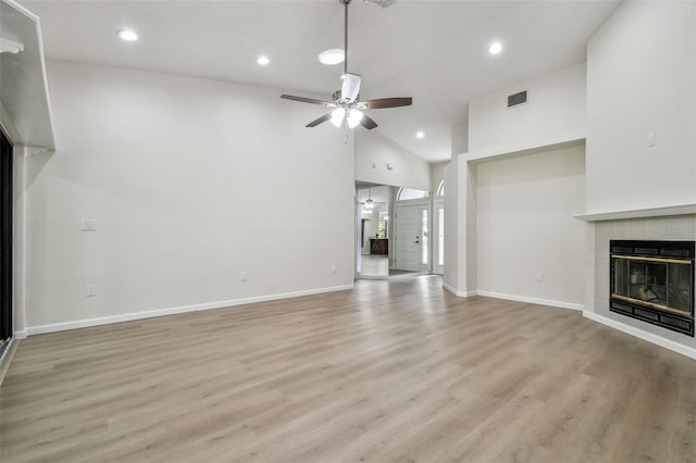 unfurnished living room featuring a tiled fireplace, high vaulted ceiling, ceiling fan, and light hardwood / wood-style flooring