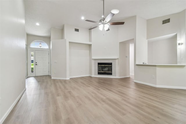 unfurnished living room featuring a tiled fireplace, a towering ceiling, ceiling fan, and light hardwood / wood-style flooring