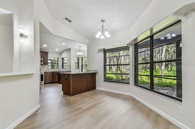 interior space featuring decorative light fixtures, lofted ceiling, a chandelier, light stone countertops, and light hardwood / wood-style flooring