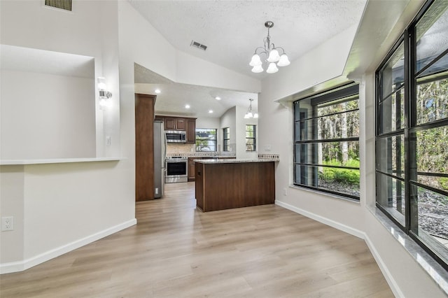 kitchen featuring vaulted ceiling, a chandelier, kitchen peninsula, stainless steel appliances, and light wood-type flooring