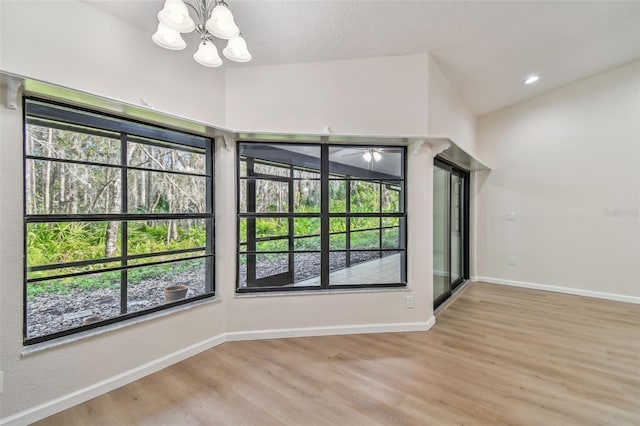 empty room featuring vaulted ceiling, plenty of natural light, an inviting chandelier, and light hardwood / wood-style floors