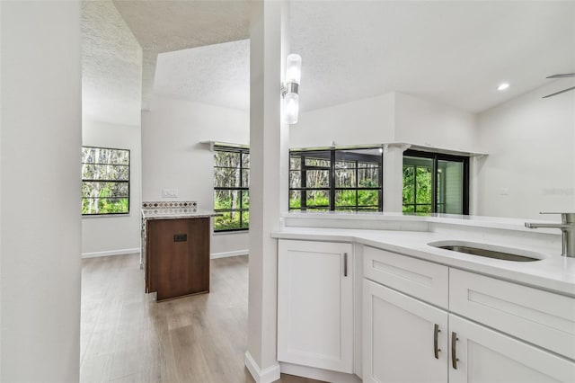 kitchen with sink, light hardwood / wood-style flooring, hanging light fixtures, a textured ceiling, and white cabinets