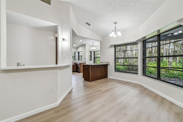 kitchen featuring lofted ceiling, pendant lighting, light hardwood / wood-style flooring, a notable chandelier, and a textured ceiling