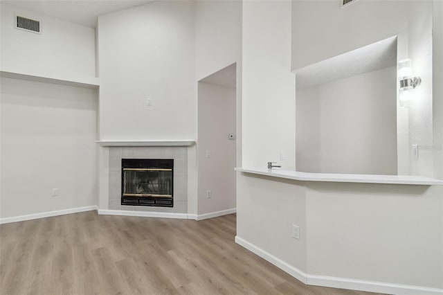 unfurnished living room featuring a high ceiling, a tile fireplace, and light hardwood / wood-style flooring