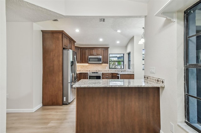 kitchen featuring appliances with stainless steel finishes, light stone counters, light hardwood / wood-style floors, a textured ceiling, and kitchen peninsula