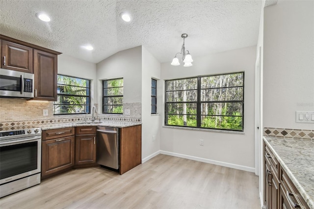 kitchen with appliances with stainless steel finishes, sink, light wood-type flooring, and decorative backsplash