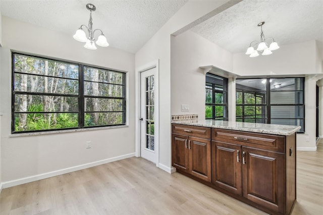 kitchen featuring light stone counters, a chandelier, a textured ceiling, light hardwood / wood-style flooring, and pendant lighting